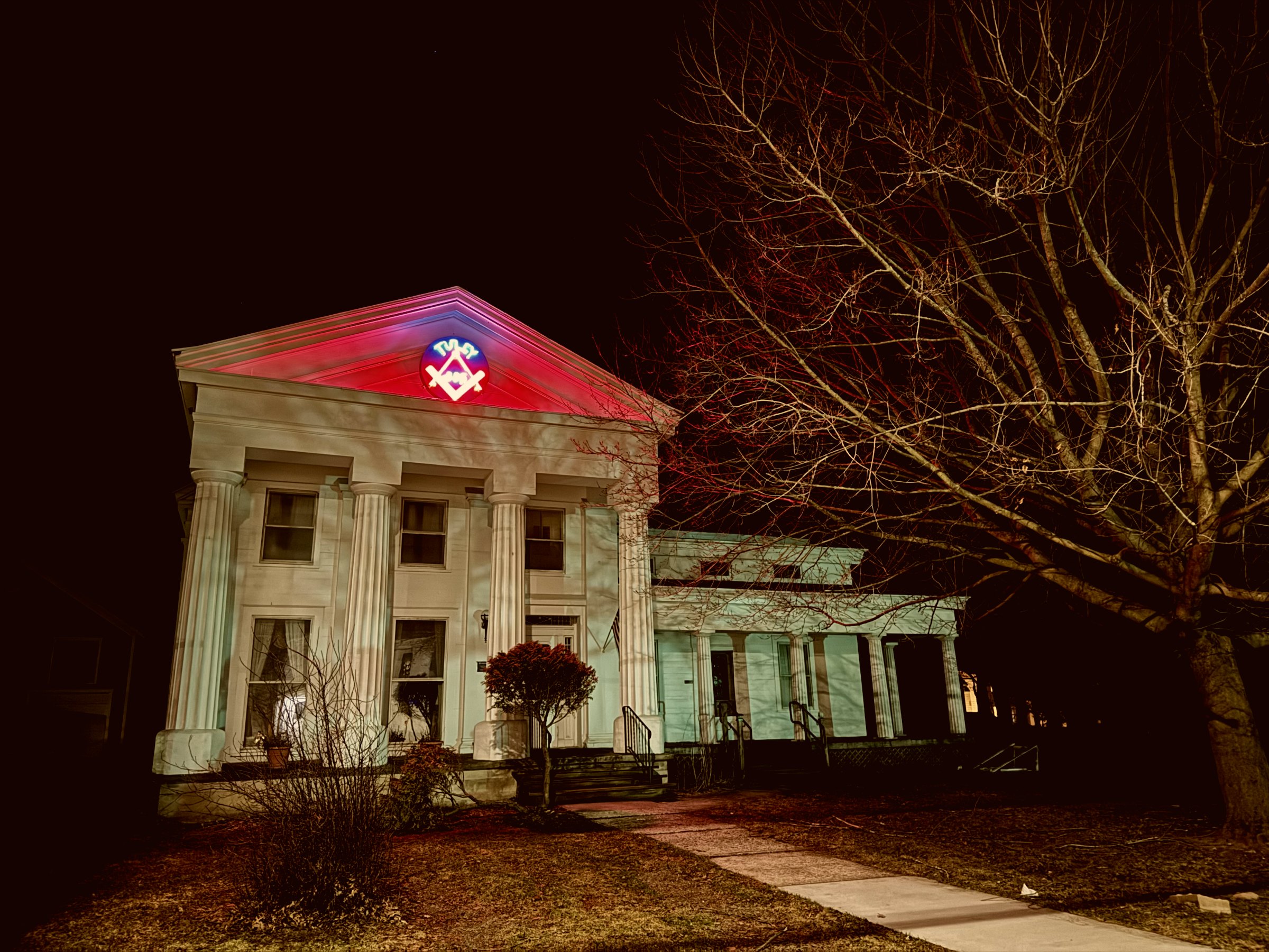 The Tully Masonic Lodge lit at night, columns rising beneath the illuminated Masonic emblem